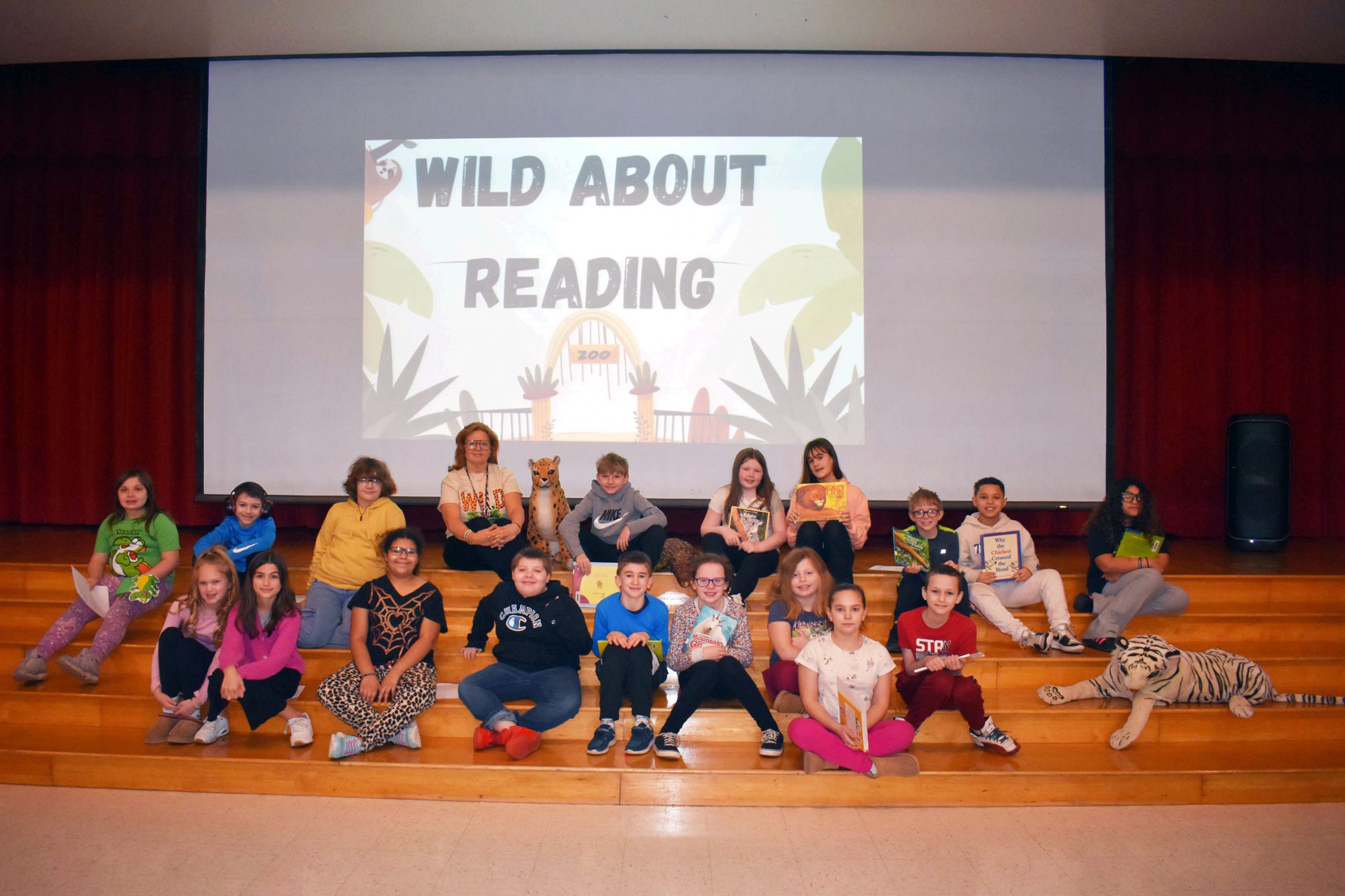 Students posing on stage with "Wild About Reading" displayed on screen behind them