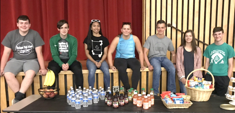 Students sit on the edge of a stage. Snack foods are in the foreground