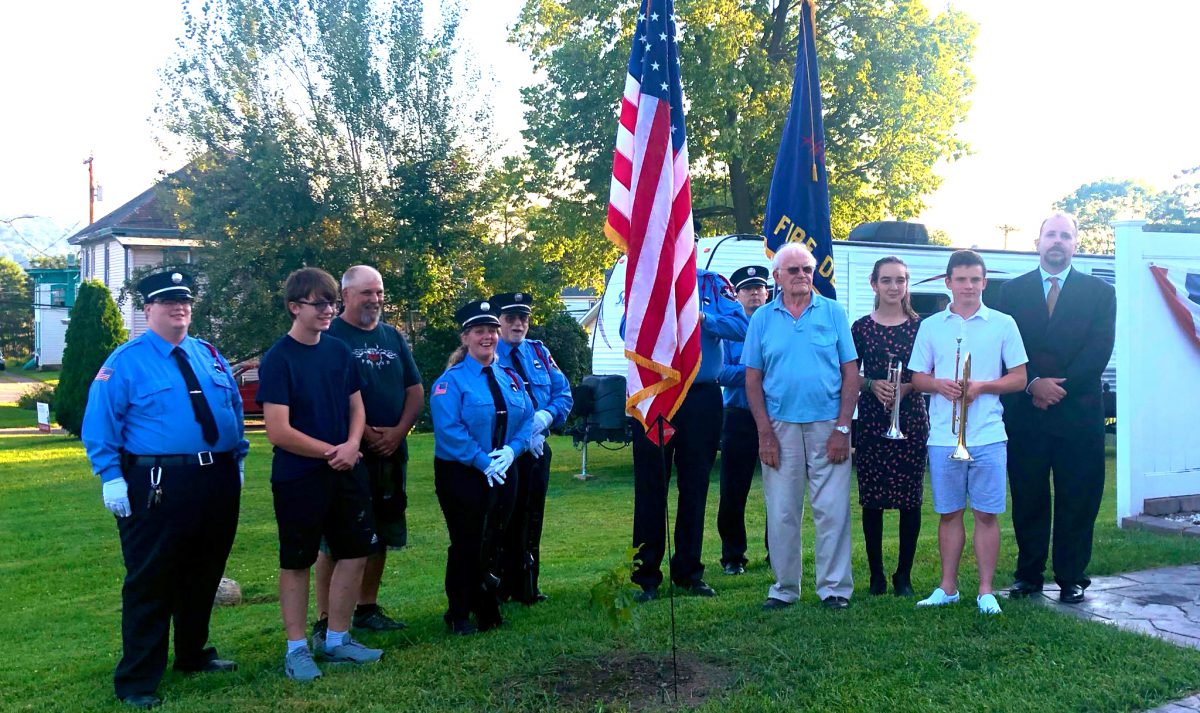 Students, police officers and others stand outdoors near an American and New York State flags