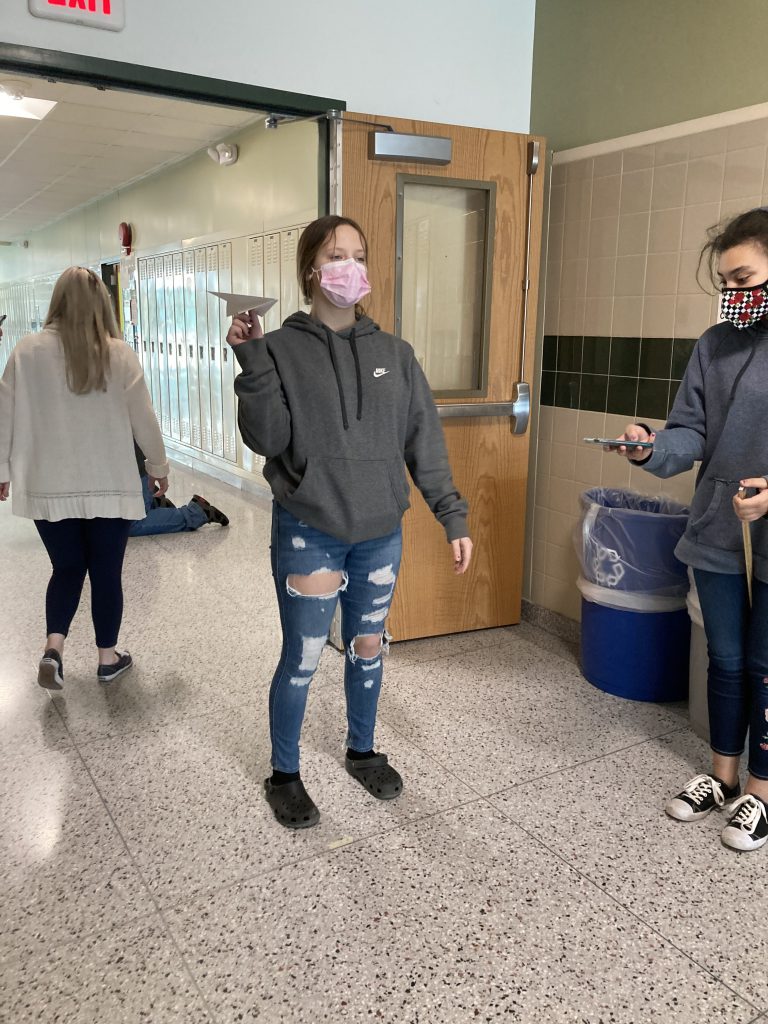 A student throws a paper airplane in a hallway 