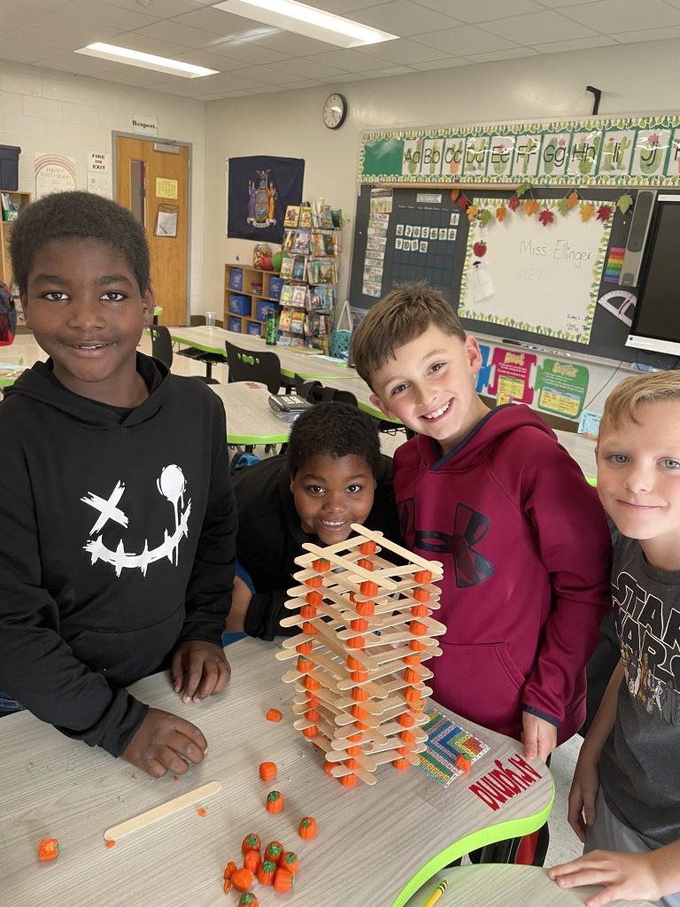 Four STEM 3 Club students pose with popsicle stick and candy corn pumpkin tower