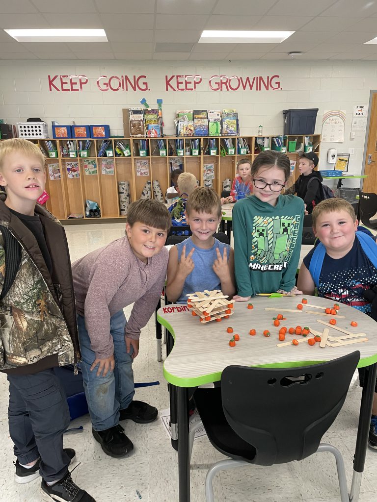 Five STEM 3 Club students pose with popsicle stick and candy corn pumpkin tower