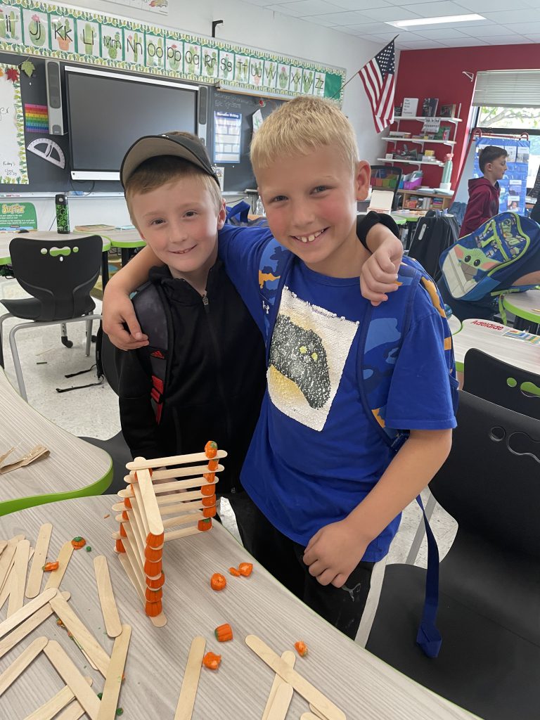 Two STEM 3 Club students pose with popsicle stick and candy corn pumpkin tower