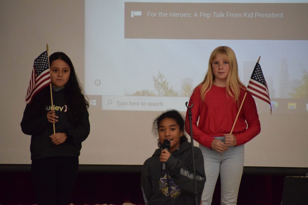 Two students holding American flags and one student leading the pledge