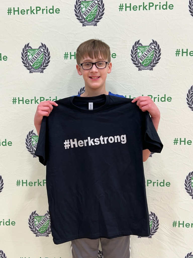 Student Logan Perri holding up a #HerkStrong shirt received for winning a PE character recognition award