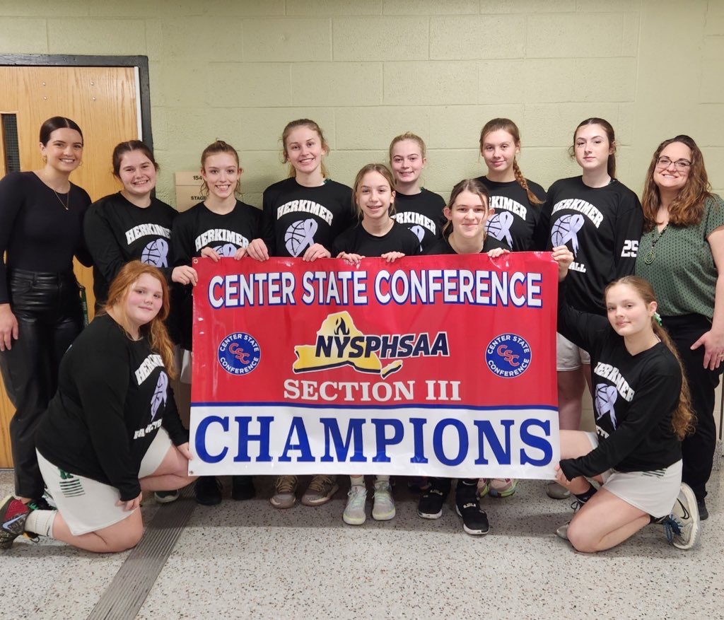 Herkimer girls varsity basketball players and their coaches hold the co-league-champions banner