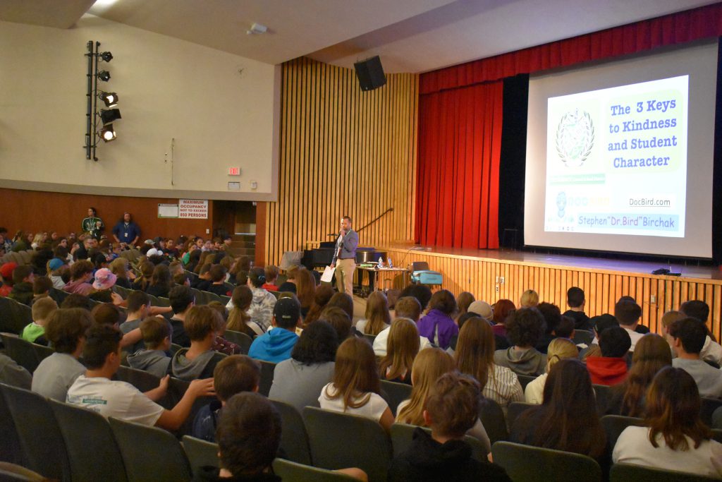 Principal Zach Abbe speaks in front of students at an assembly in the auditorium