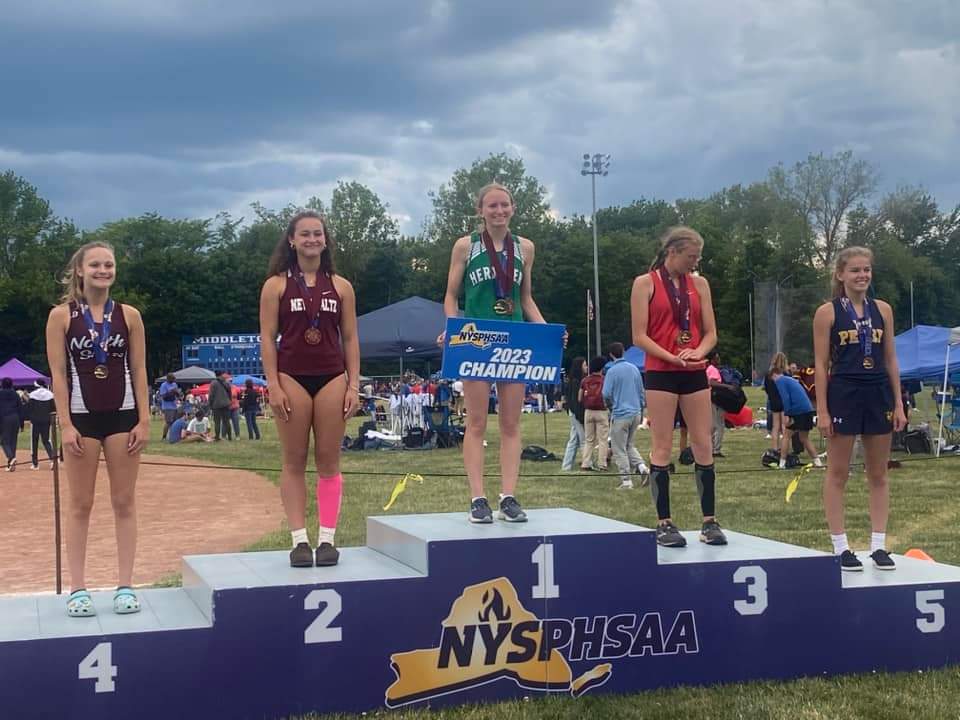 Melia Couchman holding up her 2023 state championship in pole vault sign on the medal stand next to other students