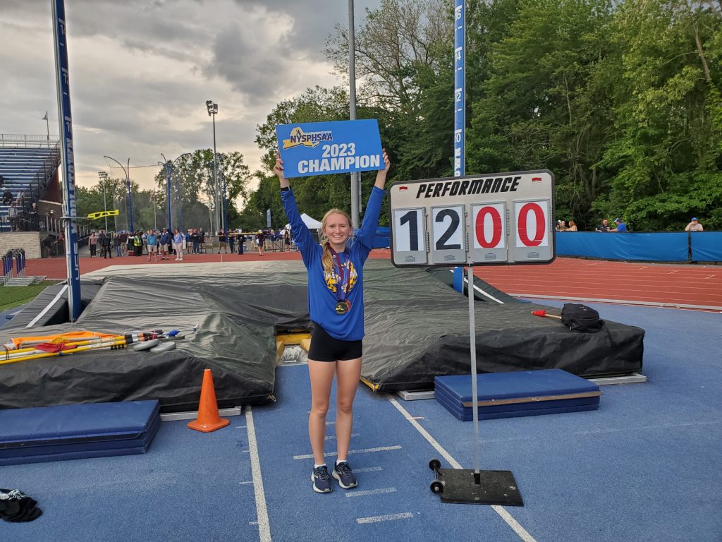 Melia Couchman holding up her 2023 state championship in pole vault sign next to a sign displaying 1200