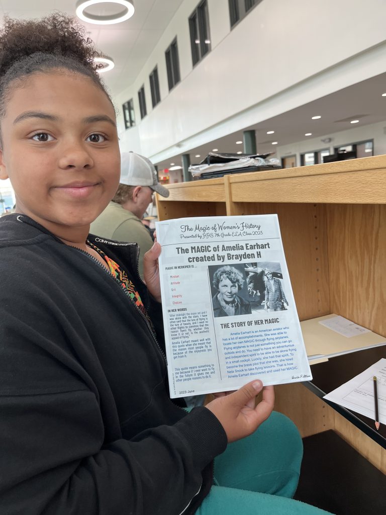 Seventh grade officer holding up a printed newspaper from a project about the magic of women's history