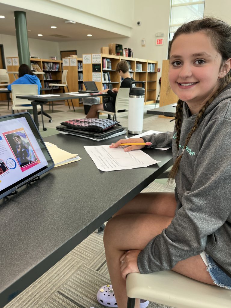 Seventh grade officer holding up a printed newspaper from a project about the magic of women's history