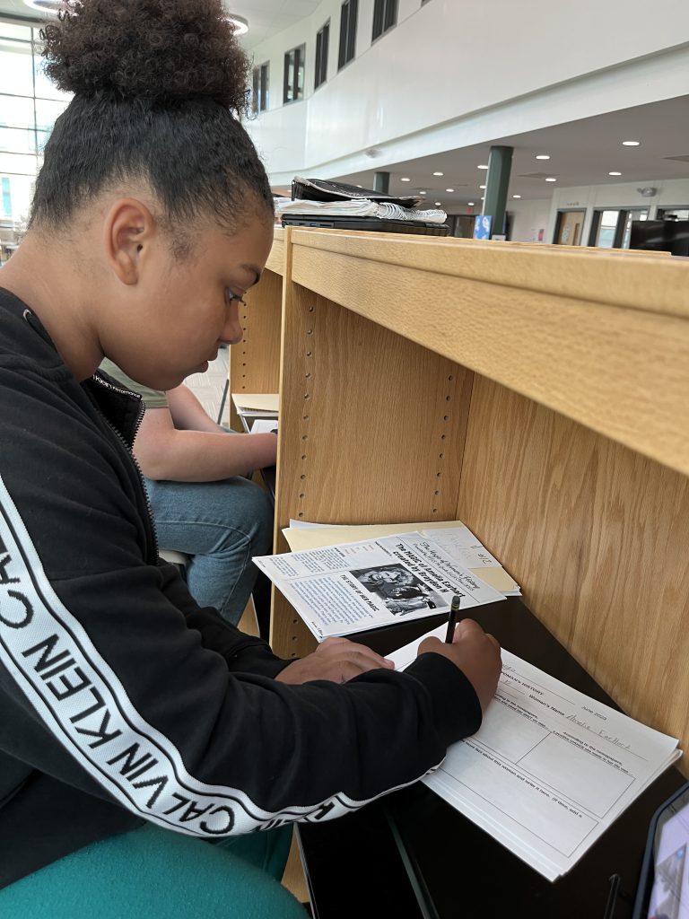 Seventh grade officer writing while looking at a newspaper from a project about the magic of women's history