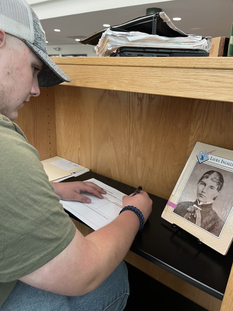 Seventh grade officer writing while looking at a newspaper from a project about the magic of women's history