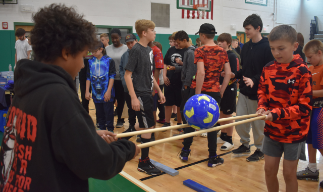 Two students balancing a soccer ball on sticks