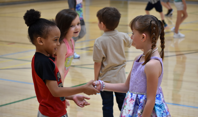 Students shaking hands in PE class for a game of "Nice to meet you tag" as other students play behind them.