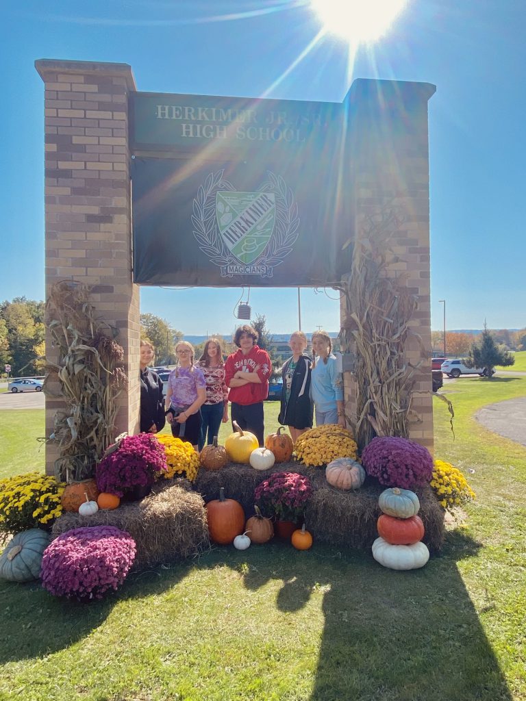 Several ag students pose by high school sign and fall harvest design