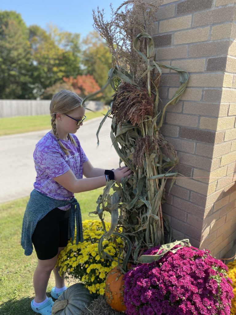 Student hanging up corn stalks at high school sign