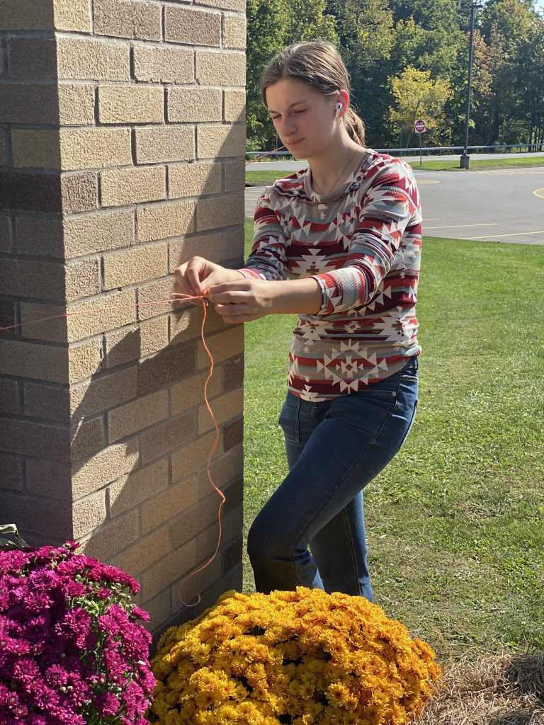 Student working on fall harvest design at high school sign