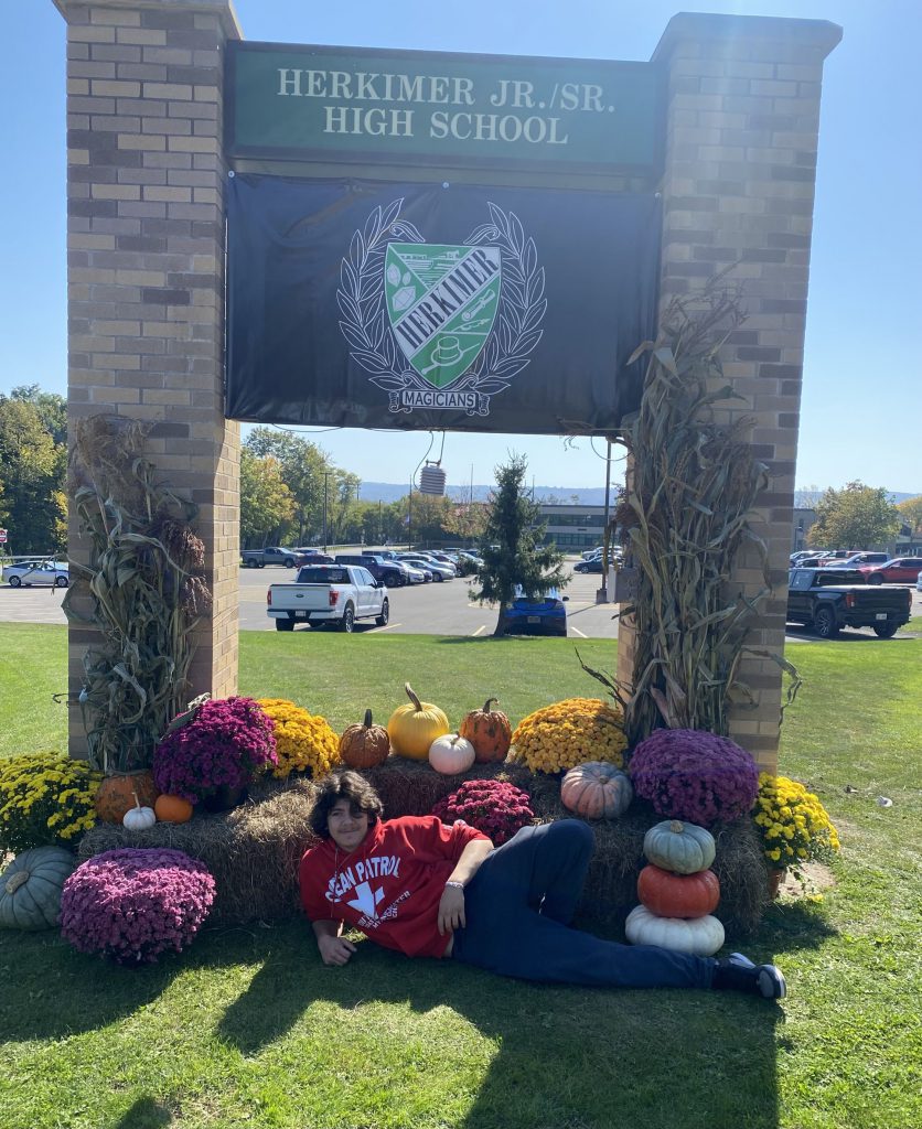 Student posing by high school sign with fall harvest design