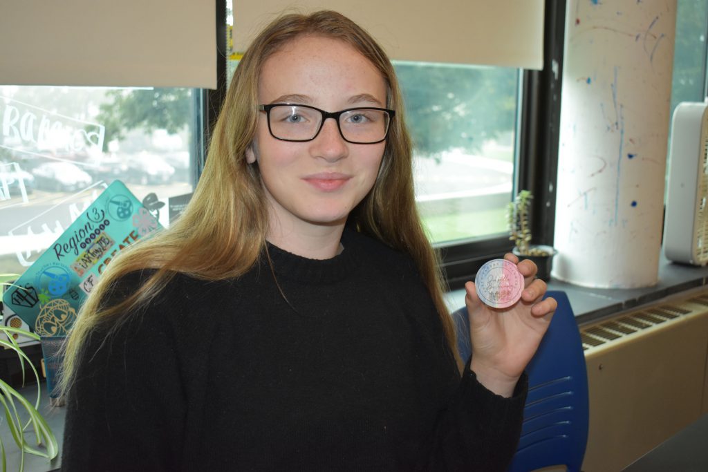 Social emotional artistic learning student holding a wood coin she designed in class