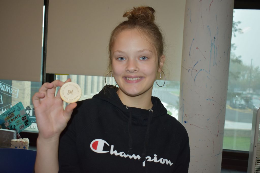 Social emotional artistic learning student holding a wood coin she designed in class