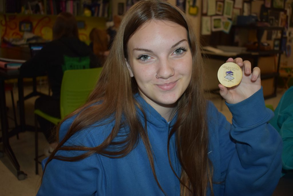 Social emotional artistic learning student holding a wood coin she designed in class