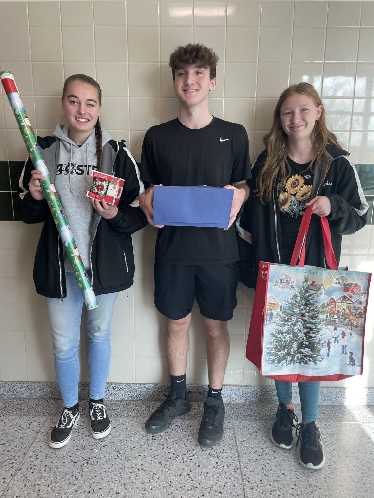 Three student organization presidents posing with Holiday Project items in the hallway