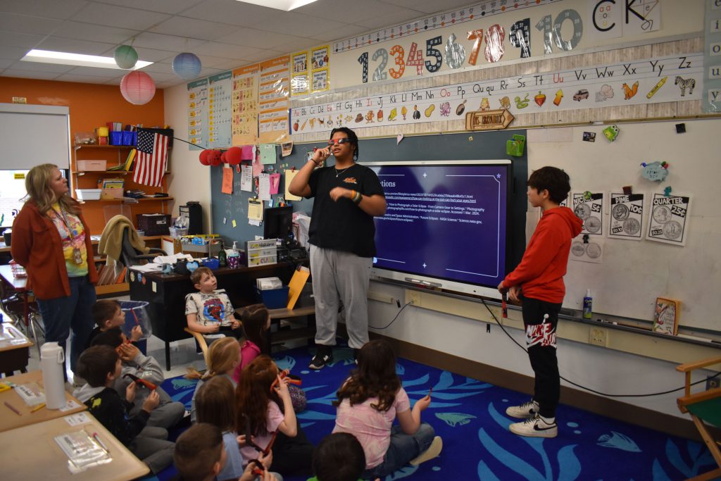 Two 10th graders demonstrating safety glasses and presenting about the eclipse to second graders