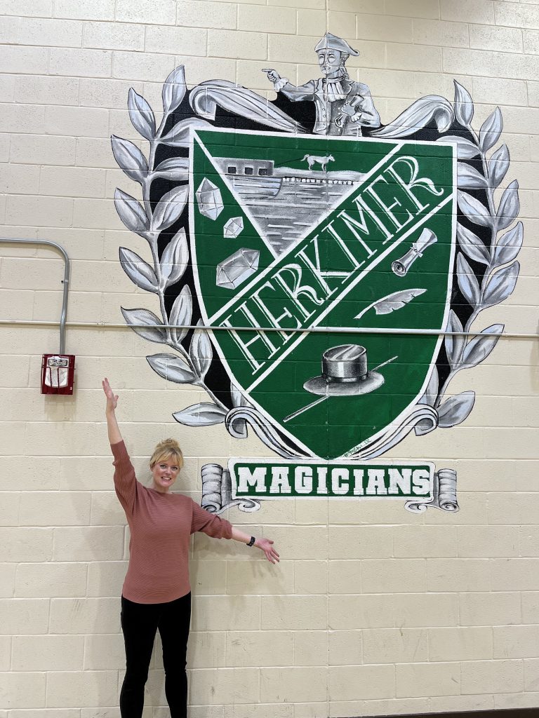 Heather Spanfelner posing by mural she painted in aux gym