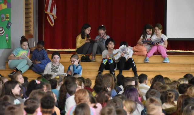 Students reading on stage during assembly