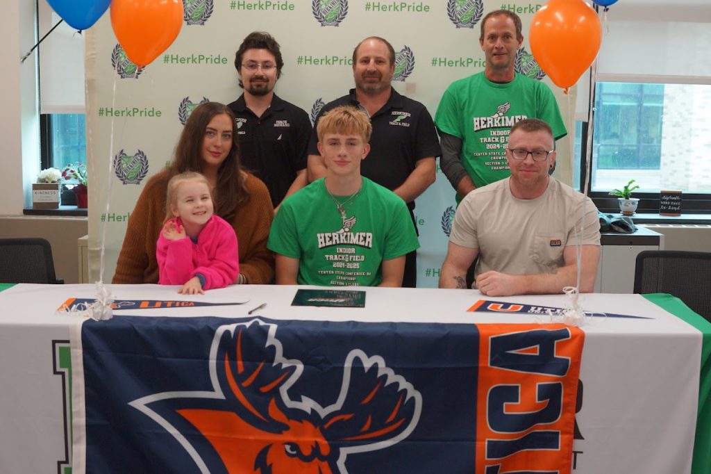 Kaleb Davis and six others at his Utica University signing with a Utica University banner on the table