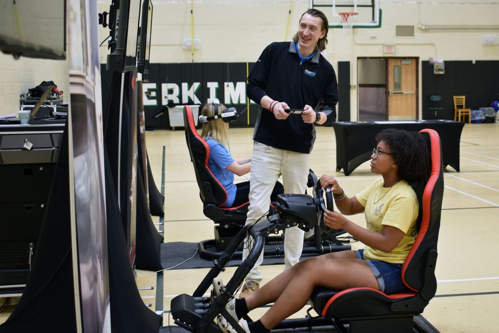Two students using Save a Life Tour VR driving setups as presenter looks on