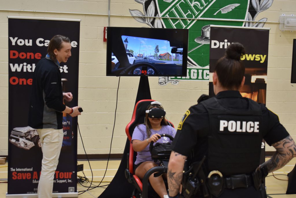 Student drives in VR as presenter and SRO look on