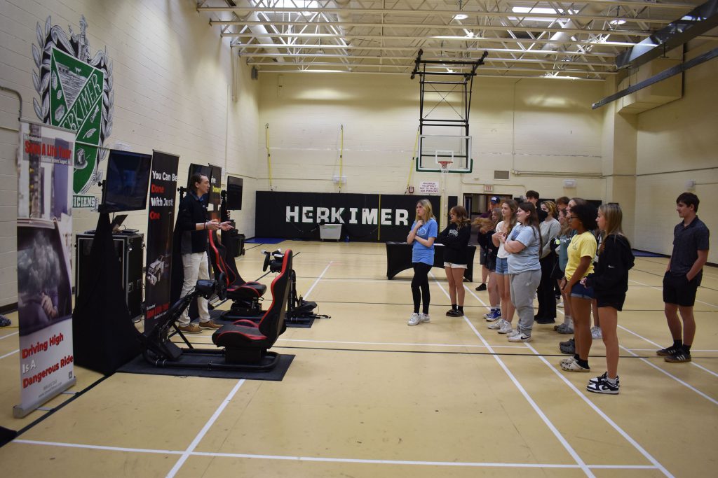 Save a Life Tour presenter stands by driving setups while talking to students in gym