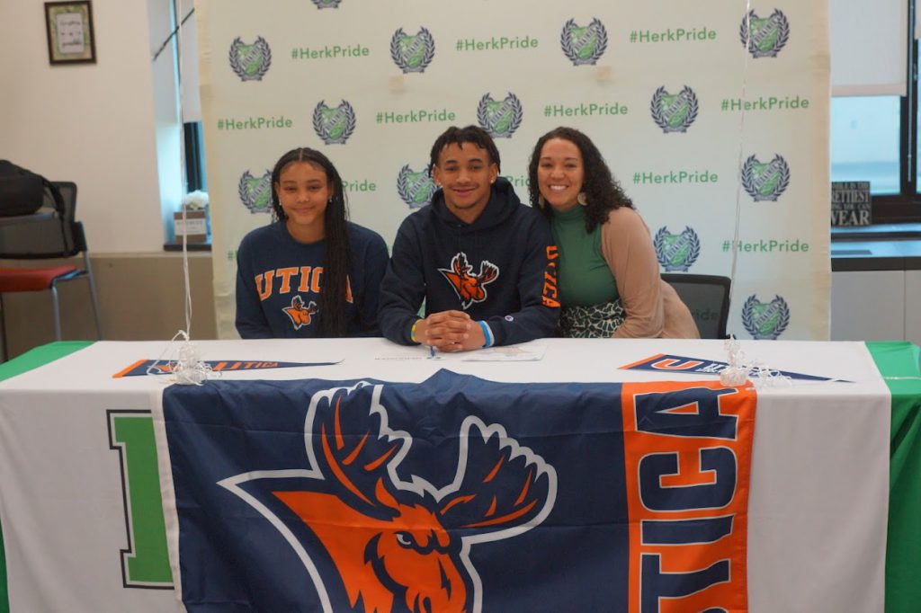 Terrance Jones and two others at his Utica University signing with a Utica University banner on the table