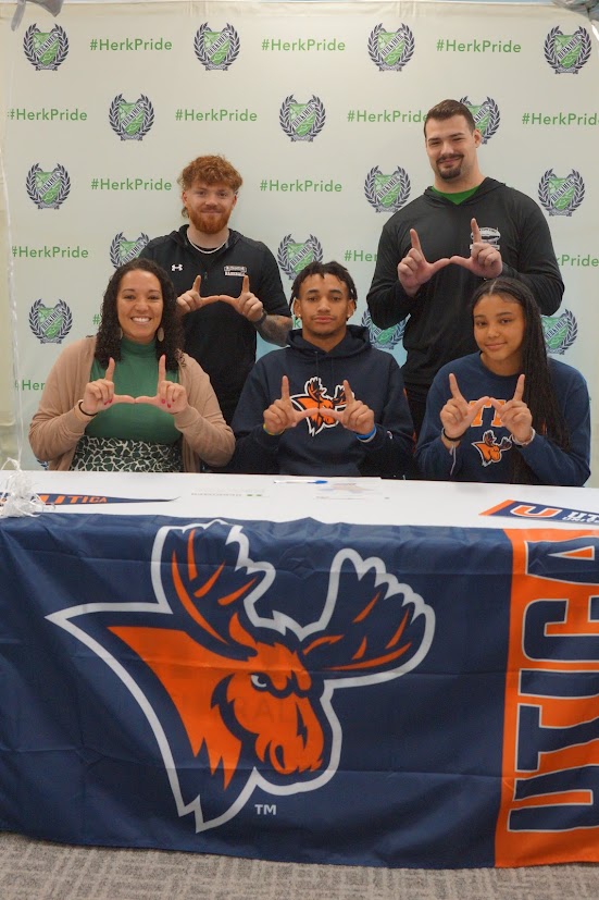 Terrance Jones and four others at his Utica University signing with a Utica University banner on the table and they're making U shapes with their hands