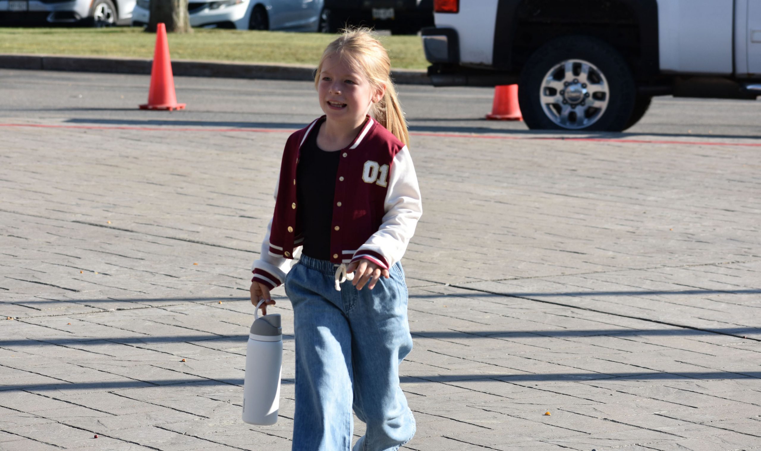 Student walking outside toward school on first day of school and carrying a water bottle