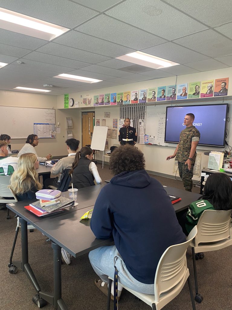 Former student in camouflage and Marine Corps Staff Sgt. speaking to students in classroom