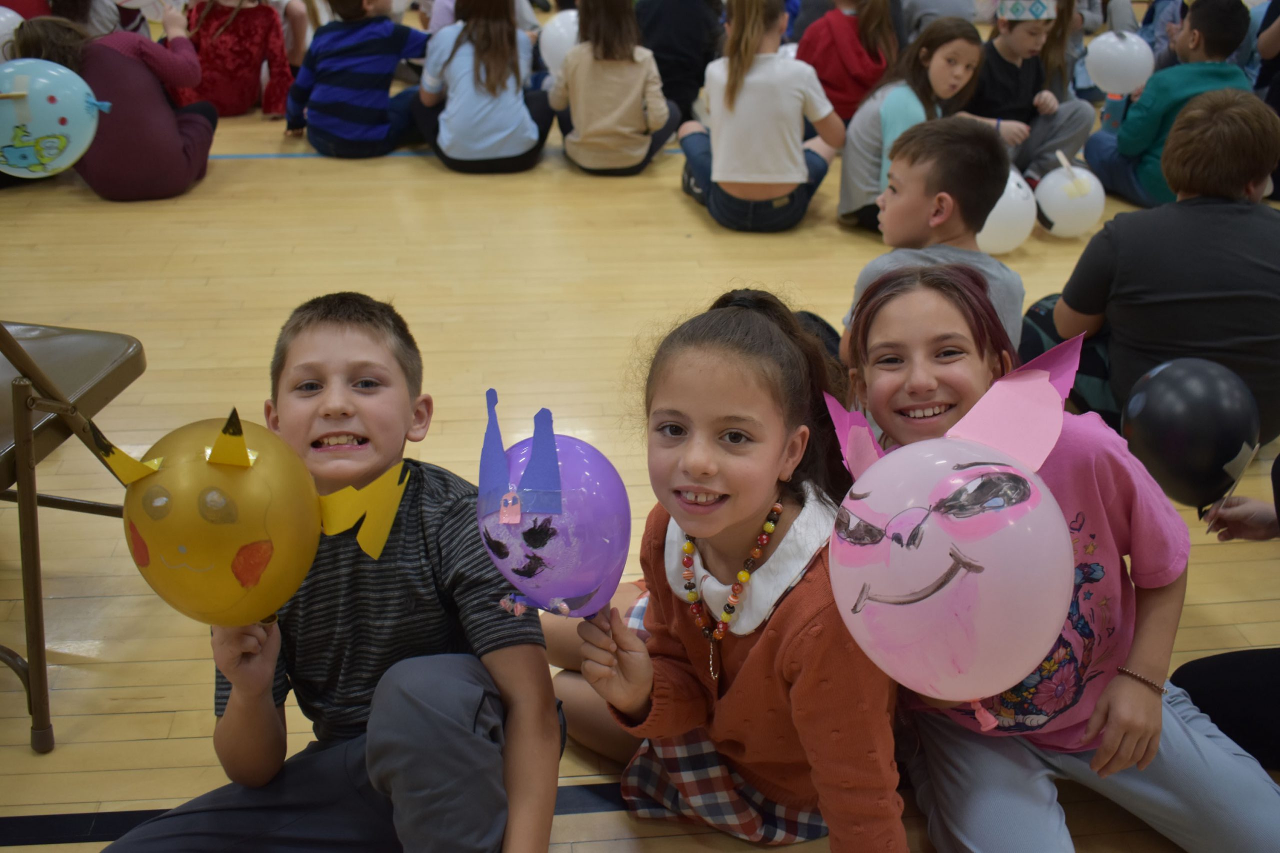 Students sitting on gym floor holding up balloons