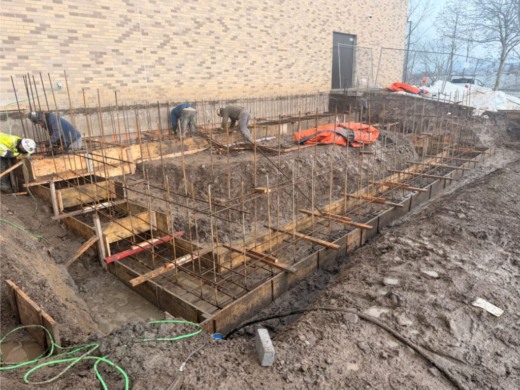 Workers working on the foundation for the gym storage addition