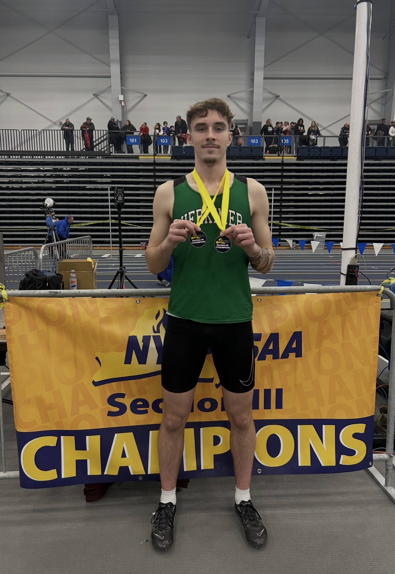 Isabella Maass wearing medals and standing by sectional championship banner