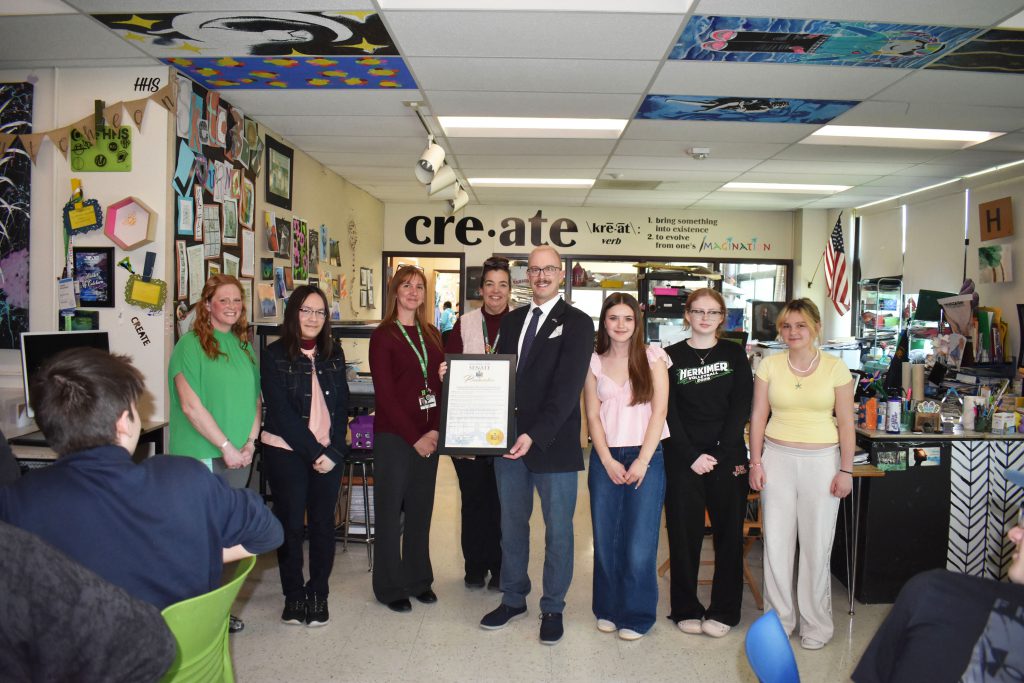 Senator, art teachers and art students posing together with proclamation in art classroom