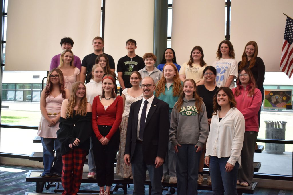 Senator posing with Show Choir students standing on risers in library