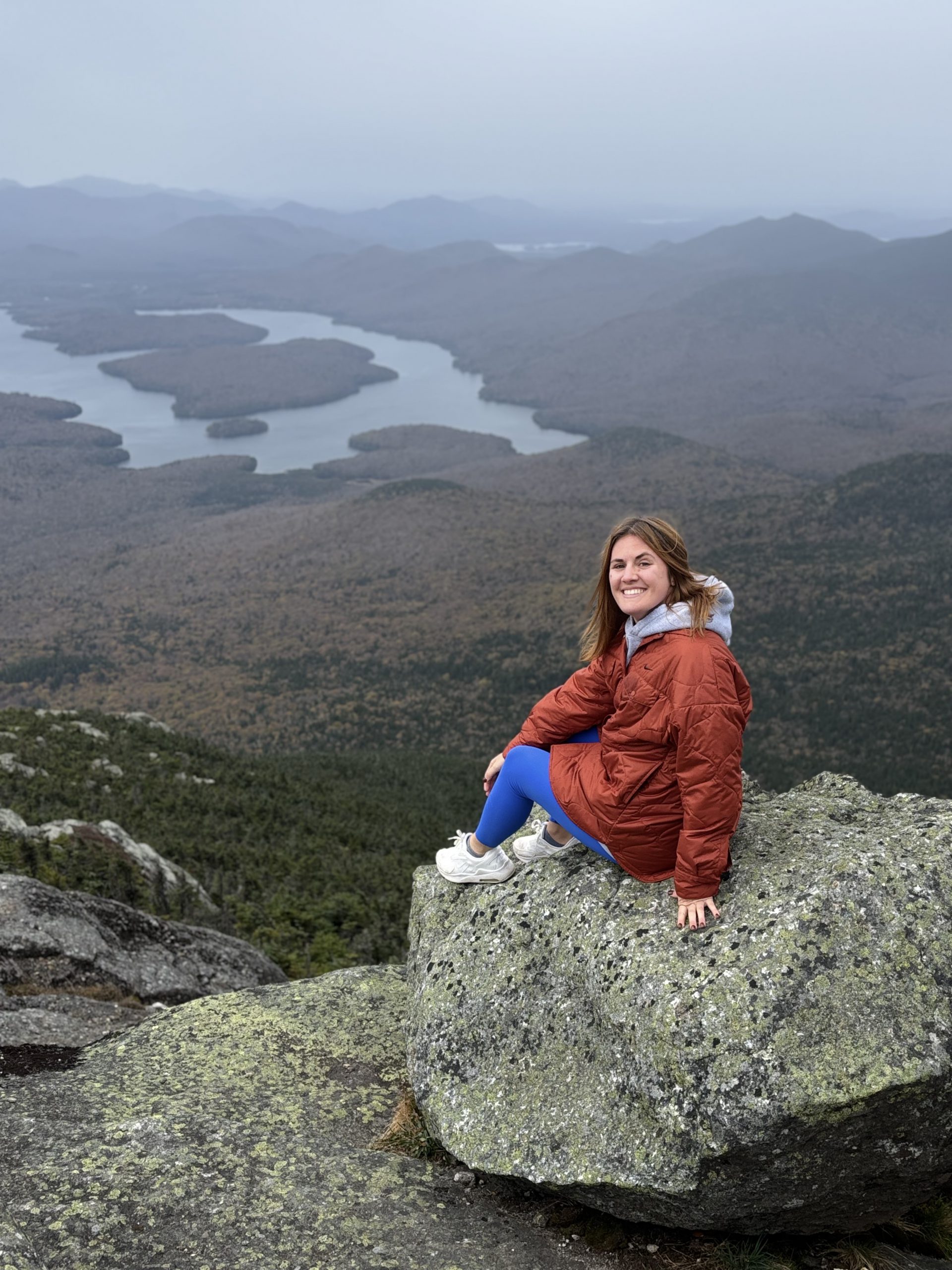 Emily Schumske sitting on large rocks above a a wide landscape with water and more