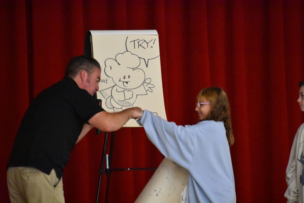 Cartoonist Duane Abel fist-bumping a student on stage