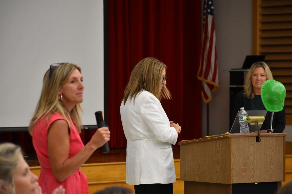 Renee Vogt speaking into microphone with Kathleen Carney and Maria Lindsay in the background