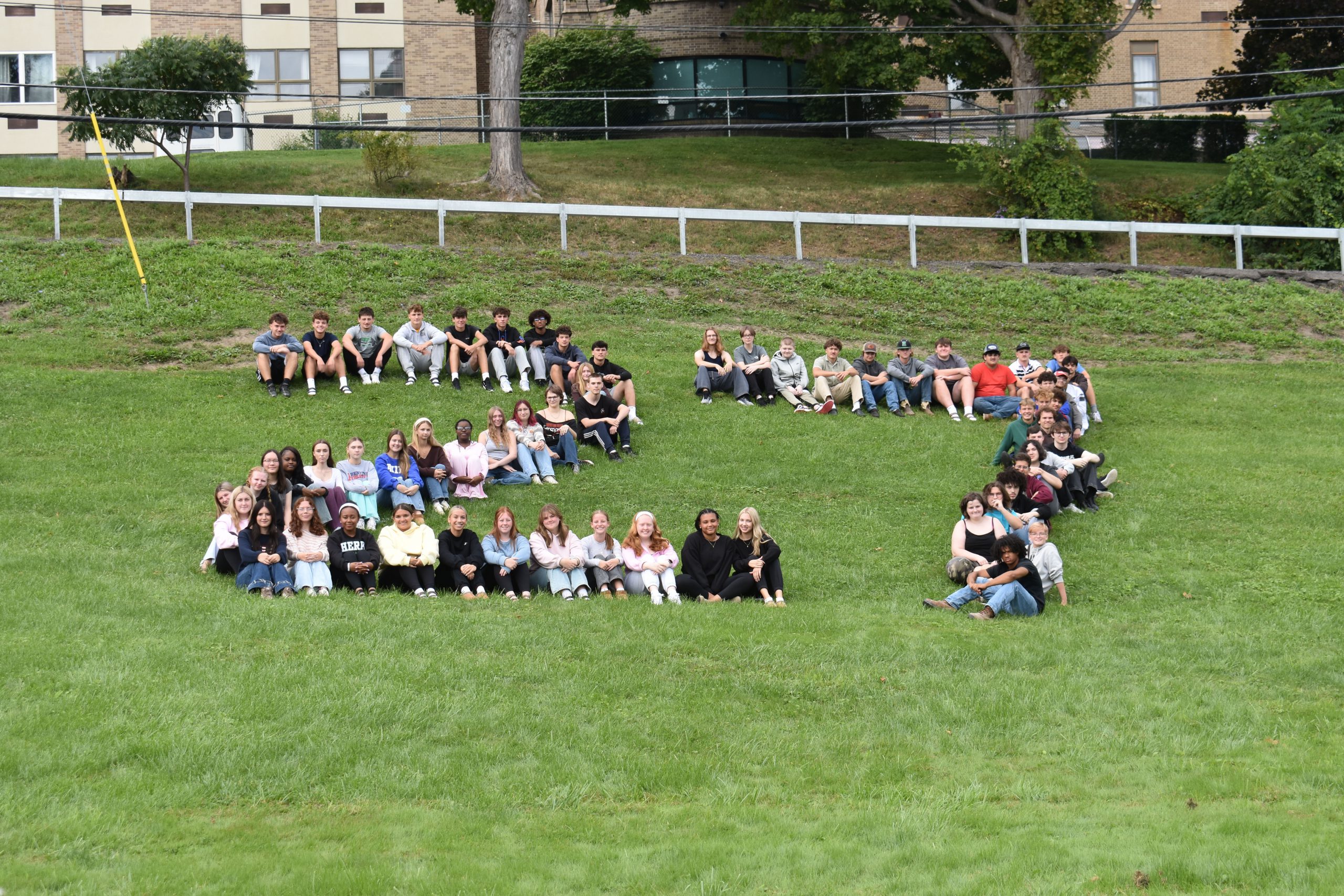 Class of 2027 posed in shape of "27" outside on grassy hill