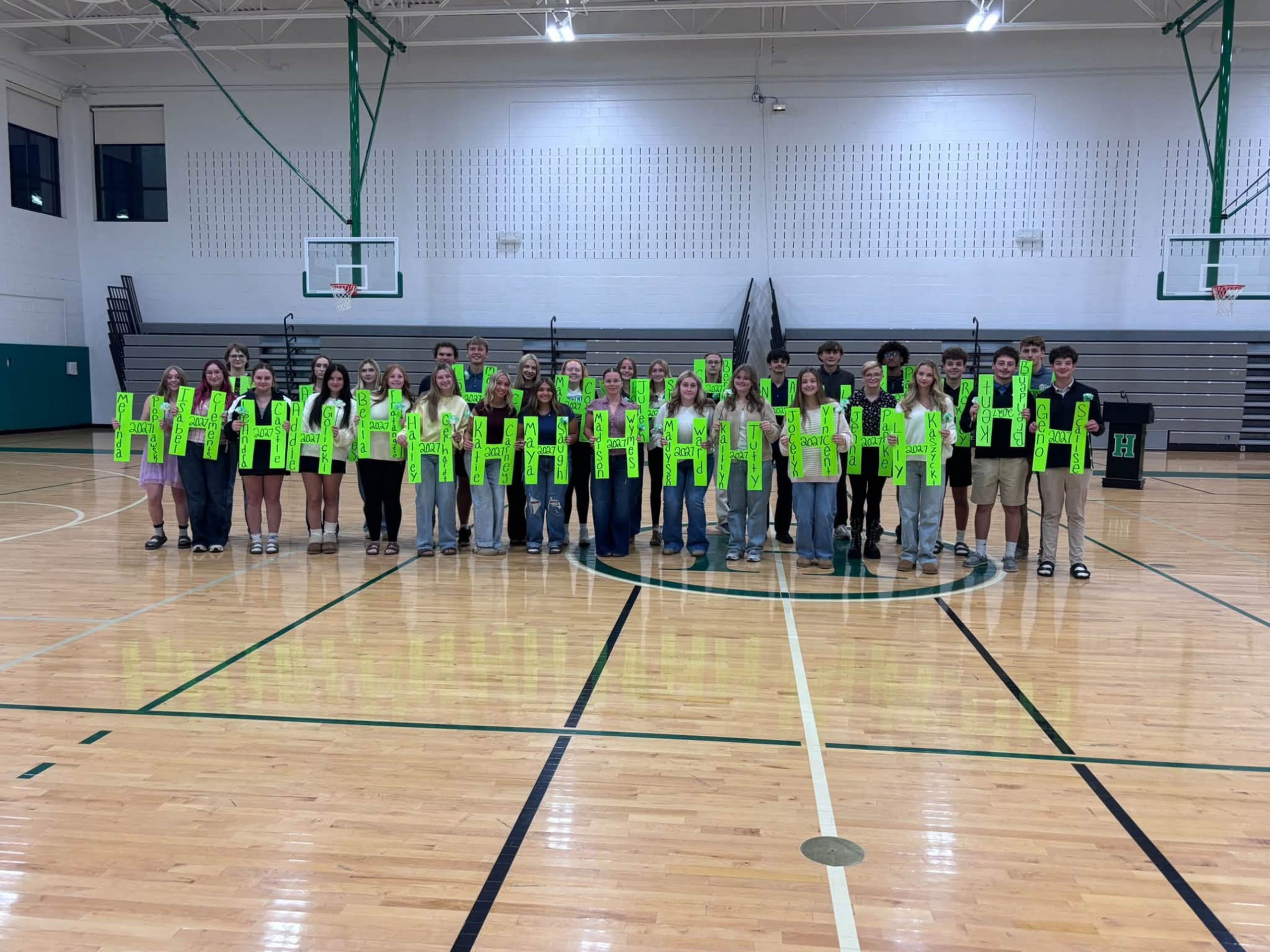 Seniors holding green Hs in gym